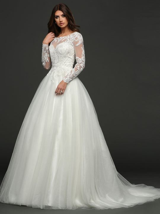 A woman in the “Victoria” ivory wedding dress by Avery Austin, featuring long sleeves, lace details, a full tulle skirt, and a ball gown silhouette, stands against a dark background.