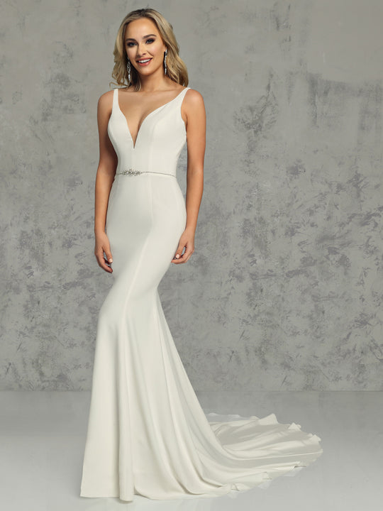 A woman stands against a textured gray background, smiling with her hands by her sides, wearing the Avery Austin Aria - Tried On Sample: a sleeveless, fitted crepe fit-and-flare wedding dress with a deep V-neckline and jeweled belt.
