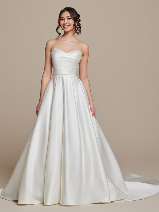 A smiling woman models the averyaustin Rosie strapless satin wedding dress in ivory, featuring a fitted bodice, full skirt, and elegant long train against a plain beige background.