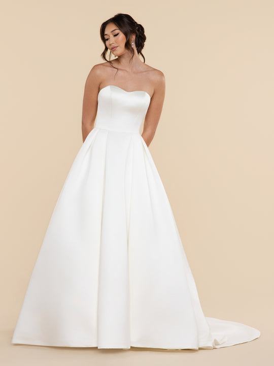 A woman wearing the Odette averyaustin ivory-colored, strapless A-line wedding dress with a sweetheart neckline and a full satin ball gown skirt.