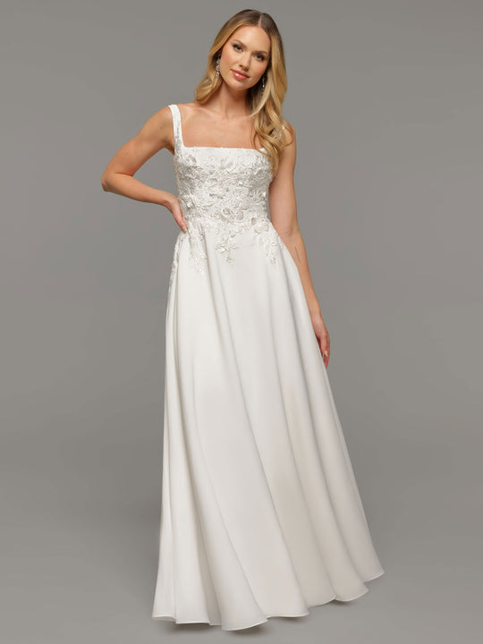 A woman models the Scarlett wedding dress by averyaustin, featuring an A-line silhouette, square neckline, lace bodice, and satin skirt. She has long blonde hair and wears drop earrings against a plain grey background.