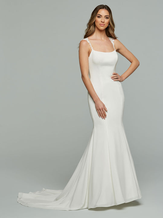 A woman poses gracefully in the Avery Austin Whitley wedding dress, an elegant ivory gown with a square neckline, thin straps, fitted backless design, and a long, flowing train. Her wavy hair cascades down as she smiles gently.