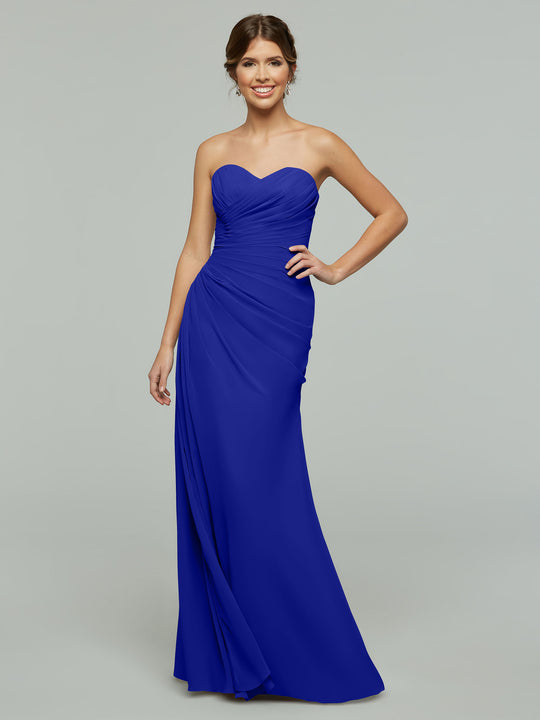 A woman wearing Avery Austin’s 80028— a strapless, floor-length chiffon dress with a sweetheart neckline—smiles with one hand on her hip against a plain light gray background.
