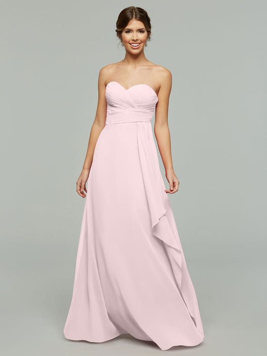 A woman wearing Avery Austin's 80046—a timeless, strapless chiffon blush pink dress with a sweetheart neckline and elegant draping—stands against a plain gray background.