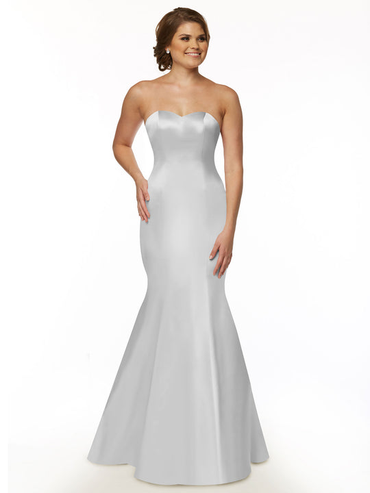 A woman stands against a plain white background wearing Avery Austin's floor-length, fitted strapless bridesmaid dress (style 80072), a white gown with a slight flare at the bottom.