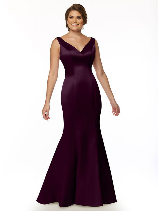 A woman stands smiling against a plain white background wearing Avery Austin style 80078—a sleeveless, floor-length deep plum fit and flare mermaid gown with a V-neckline.