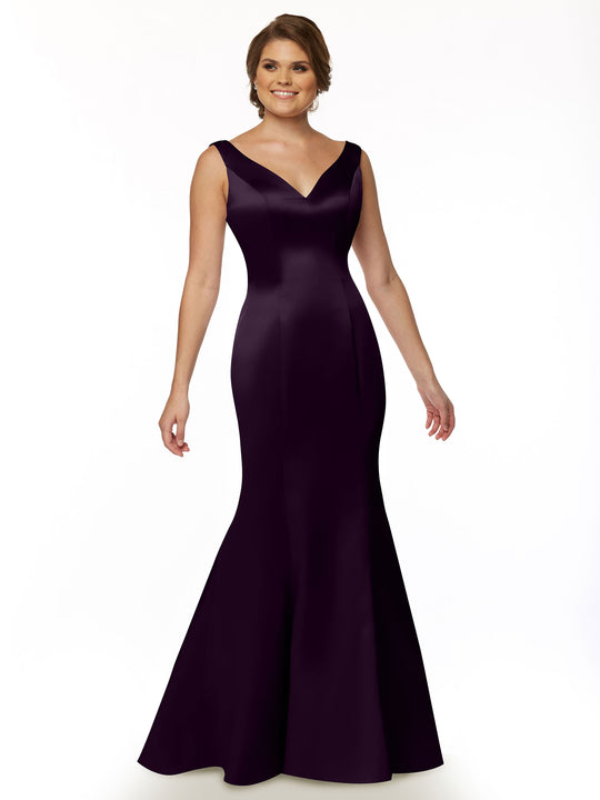 A smiling woman stands against a plain white background wearing Avery Austin style 80078, a sleeveless, floor-length deep purple fit and flare evening gown with a V-neckline and ruffled back.