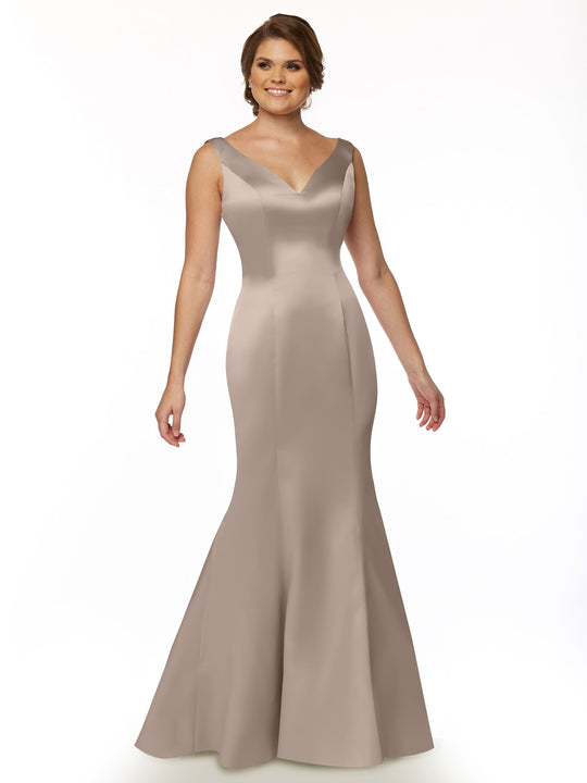 A woman wears Avery Austin’s 80078, a sleeveless, form-fitting taupe satin gown with a V-neckline and ruffled back, floor-length, as she stands and smiles against a white background.