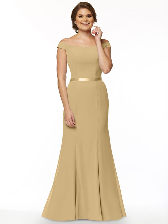A woman smiles against a white background wearing Avery Austin style 80079, a champagne off-the-shoulder, floor-length chiffon bridesmaid dress with a fitted bodice and satin waistband.