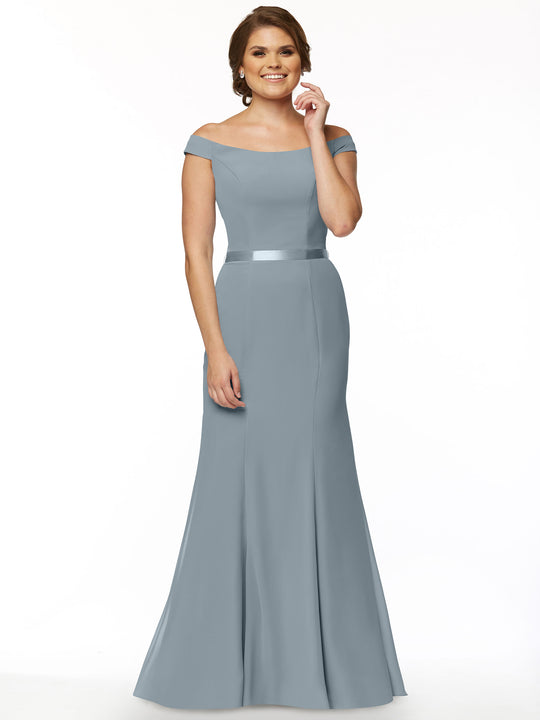 A woman smiles against a white background, wearing Avery Austin’s 80079 off-the-shoulder, floor-length bridesmaid dress in Dusty Blue chiffon with a fitted bodice and flared skirt.