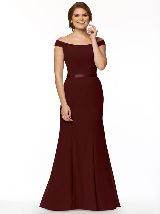 A woman in the Avery Austin 80079, a floor-length off-the-shoulder bridesmaid dress in Merlot chiffon, stands against a white background, smiling with one hand by her side and the other near her waist.