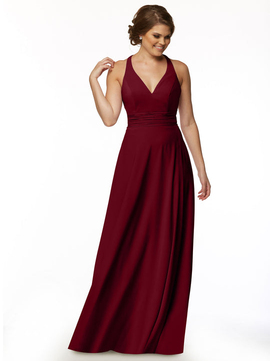 A woman wearing Avery Austin’s 80107, a sleeveless, floor-length deep red A-line dress with a feminine V-neckline and fitted waist, stands against a white background, smiling and looking to the side.