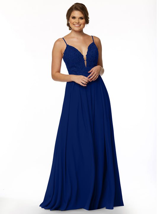 A woman wearing Avery Austin style 80113—a sleeveless deep blue gown with a fitted lace bodice, plunging neckline, and flowing A-line chiffon skirt—smiles against a plain white background.