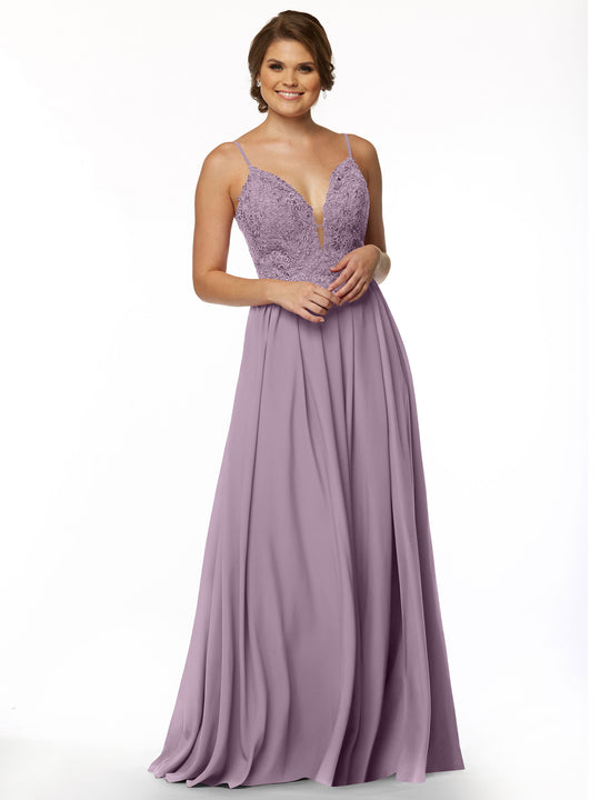 A smiling woman with short hair wears Avery Austin's 80113, a sleeveless, floor-length lavender gown featuring an A-line chiffon skirt, lace bodice, and illusion plunge neckline. The background is plain white.