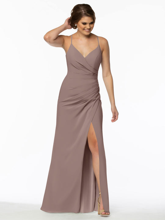 A woman stands smiling in the Avery Austin 80114 sleeveless mauve v-neck bridesmaid dress with a wrap bodice and high slit, touching her hair and wearing nude high-heeled sandals.