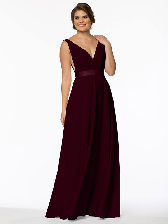A woman poses with a soft smile and hand in her hair, wearing the Avery Austin 80117, a sleeveless A-Line gown in burgundy with floor-length hem and illusion plunging sides, set against a plain white background.
