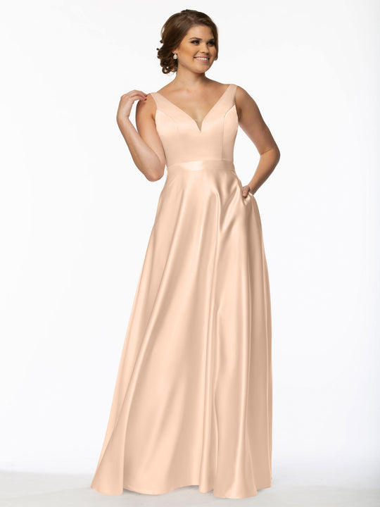 A woman smiles against a white background, wearing Avery Austin style 80118—a floor-length blush satin bridesmaid dress featuring a deep V-neckline and thin straps.