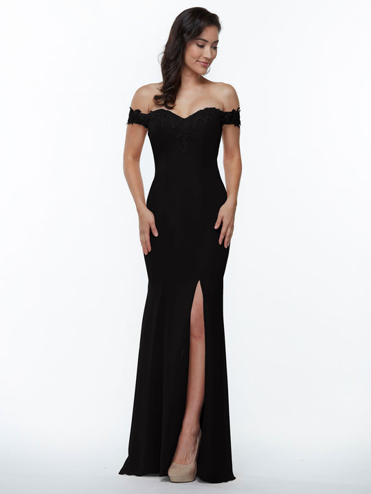 A woman wears Avery Austin style 80121, an off-the-shoulder black bridesmaid dress with a thigh-high slit and lace accents, paired with nude heels. She stands smiling against a plain white background with her hands at her sides.