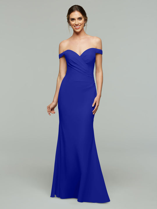 A woman wears Avery Austin’s 80122 off-the-shoulder bridesmaid dress in cobalt, featuring a floor-length skirt, as she smiles against a plain light gray background.