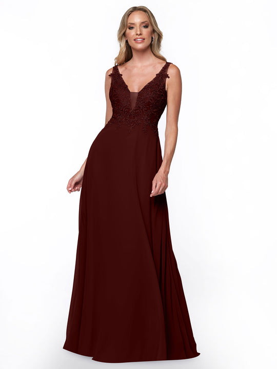 A woman in the Avery Austin 80128 merlot bridesmaid dress with a sleeveless lace bodice and V-neckline stands against a white background, smiling subtly and holding her floor-length chiffon skirt.