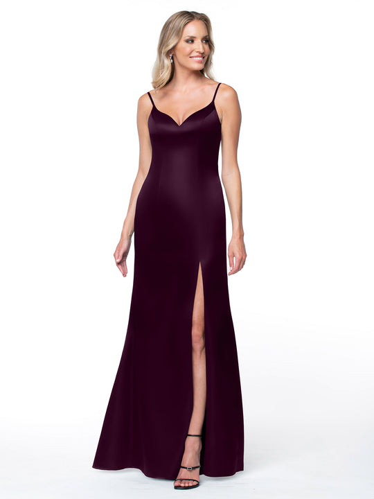 A woman models Avery Austin’s 80132: a sleeveless, floor-length deep burgundy dress with thin straps, V-neckline, intricate back, and side slit, paired with black heels against a plain white background.