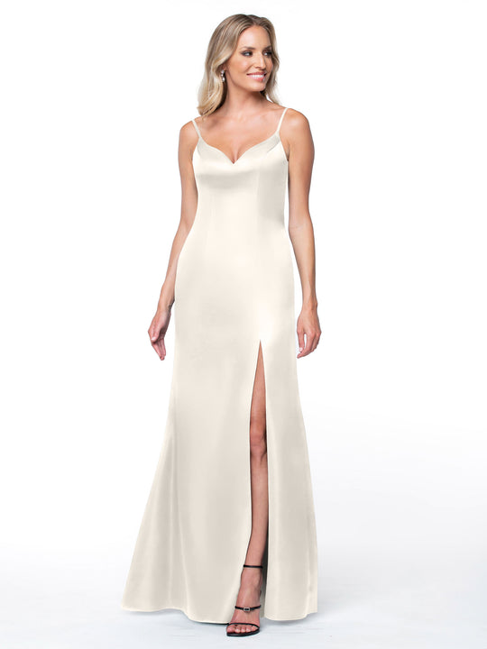 A woman stands against a plain white background wearing Avery Austin’s 80132, a sleeveless ivory satin fit and flare dress with thin straps, V-neckline, thigh-high slit, and intricate back detail.