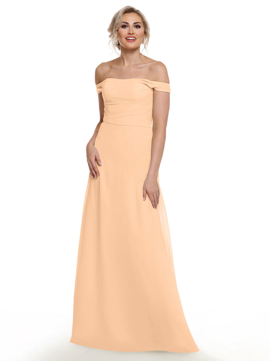 A woman models Avery Austin’s 80136, a floor-length off-the-shoulder light peach gown, smiling against a plain white background.
