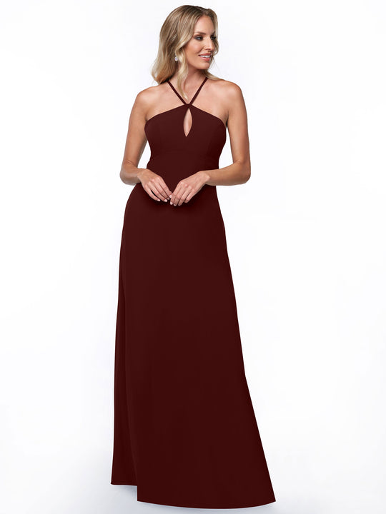 A woman smiles and looks to the side while modeling Avery Austin’s sleeveless, floor-length burgundy halter dress (style 80137) with a keyhole cutout, posed against a plain white background.