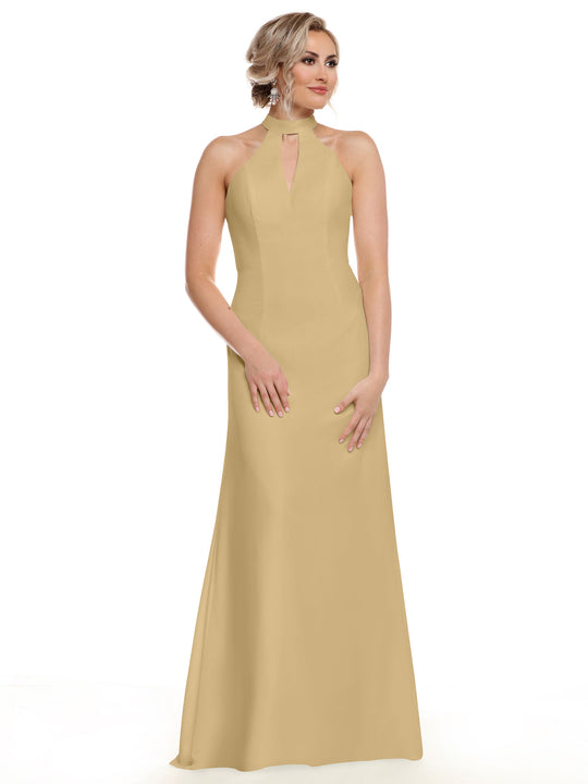 A woman poses in front of a white background wearing Avery Austin style 80138, a fitted beige floor-length gown featuring a sleeveless design, halter neckline, and keyhole cutout, with her hands relaxed and gaze slightly to the side.