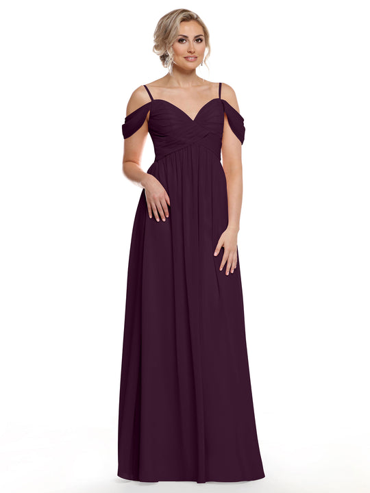 A woman models Avery Austin’s aubergine cold shoulder chiffon dress (Style 80142) featuring thin straps, a pleated bodice, sweetheart neckline, and flowing skirt, standing against a plain white background.