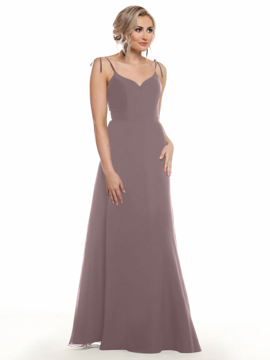 A woman with light wavy hair wears Avery Austin’s 80144: a sleeveless, mauve V-neck chiffon dress with thin straps, standing against a plain white background and looking slightly to the side.