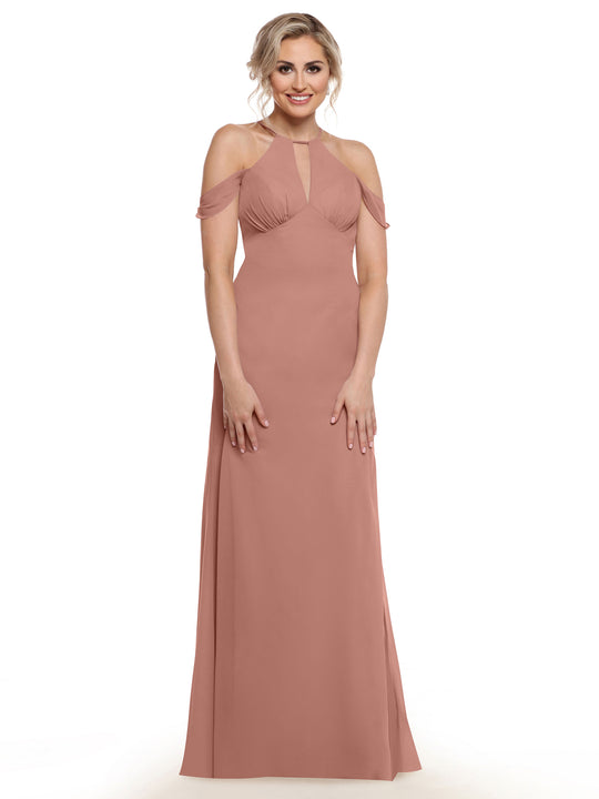 A woman wearing Avery Austin’s floor-length blush pink halter dress (Style 80148) with cold shoulder sleeves, standing and smiling against a white background.