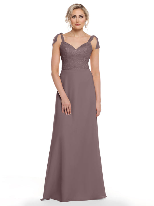 A woman in Avery Austin 80149, a mauve chiffon dress with floral lace bodice and cap sleeves, stands against a white background looking relaxed.