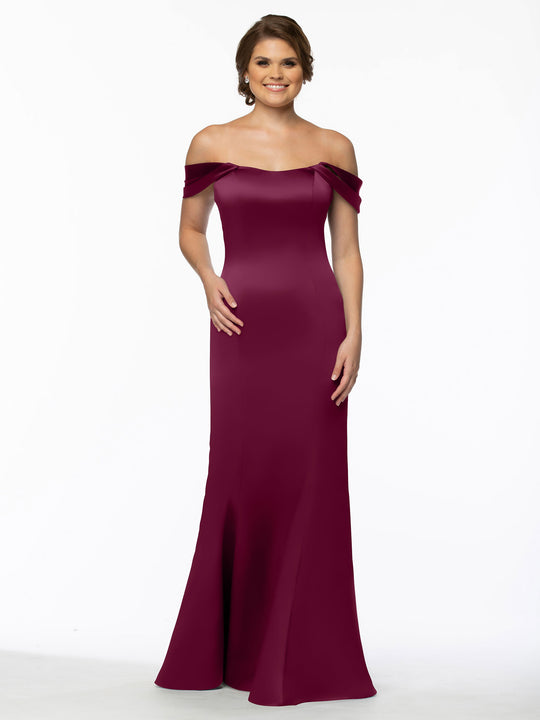 A woman stands smiling in front of a plain white background, wearing the Avery Austin 80151 floor-length, off-the-shoulder dress in deep burgundy. The fitted bodice flows into a slightly flared hem, creating an elegant silhouette.
