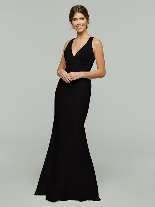 A woman with brown hair in an updo smiles while wearing the Avery Austin 80155, a sleeveless, floor-length black chiffon dress with a V-neckline and keyhole back, standing against a light gray background.