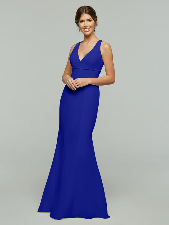 A woman smiles in the Avery Austin 80155, a floor-length sleeveless chiffon dress in cobalt with a V-neckline and keyhole back. Her hair is styled in a low updo as she poses against a plain light gray background.