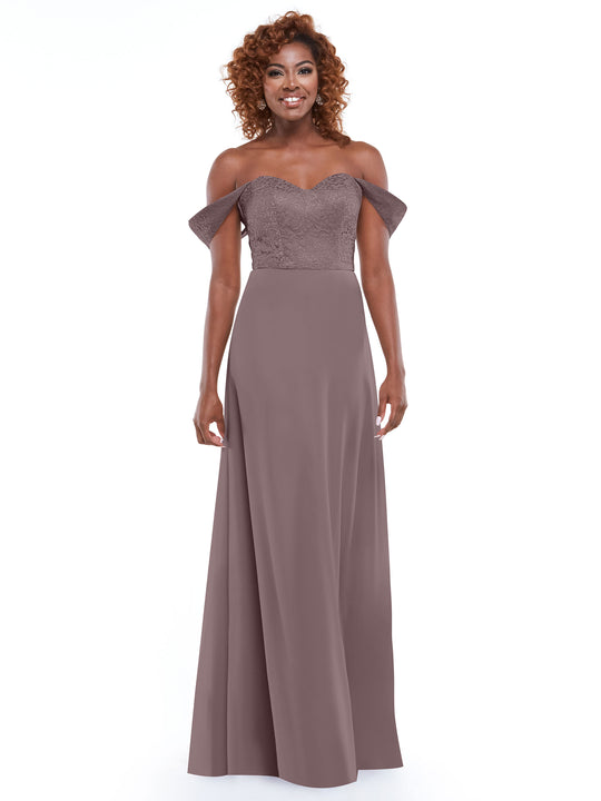 A woman stands smiling in front of a white background, wearing Avery Austin’s style 80164: a mauve off-the-shoulder dress featuring a delicate lace bodice and flowing chiffon skirt.