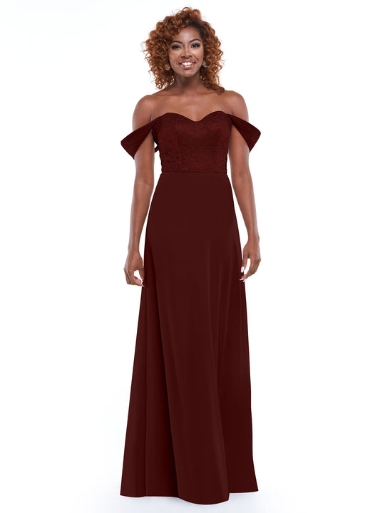 A woman with curly hair stands smiling against a white background, wearing Avery Austin style 80164—a burgundy off-the-shoulder dress with a fitted lace bodice and flowing chiffon skirt.