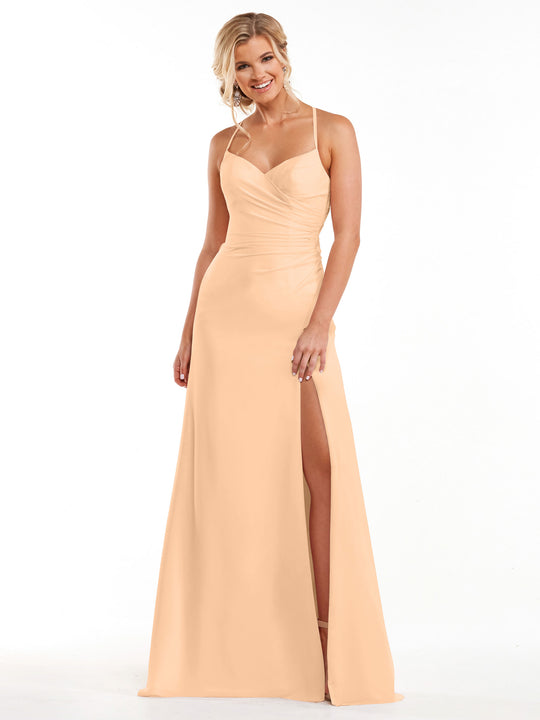 A woman wearing the Avery Austin 80167 blush floor-length ruched chiffon bridesmaid dress with thin straps, a sweetheart neckline, and a high slit stands smiling against a plain white background.