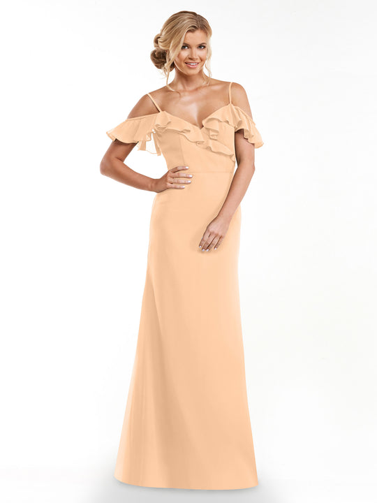 A woman smiles against a white background, modeling Avery Austin’s 80172: a long, peach A-line dress with off-the-shoulder sleeves and a ruffled neckline.