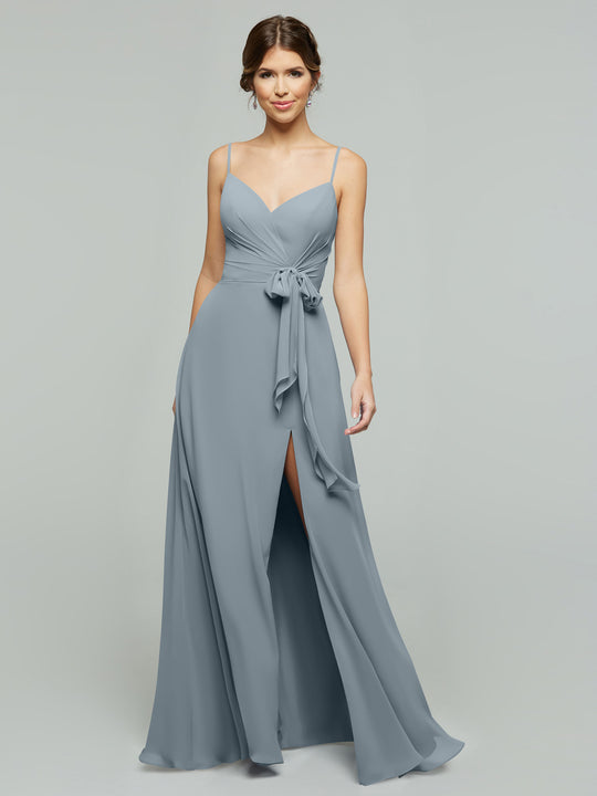 A woman models the averyaustin 80182 light blue A-line chiffon dress with thin straps, V-neckline, tied waist sash, and high side slit, standing before a plain light gray background.