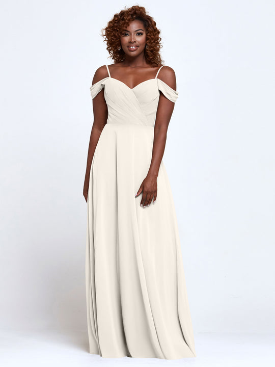 A woman stands smiling against a white background in Avery Austin’s 83003, an elegant, off-the-shoulder, floor-length ivory bridesmaid dress that exudes timeless grace.
