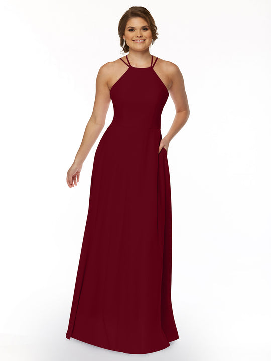 A woman smiles against a white background wearing Avery Austin’s 83006—a sleeveless, floor-length, burgundy A-line dress with a halter neckline, thin straps, and pockets.