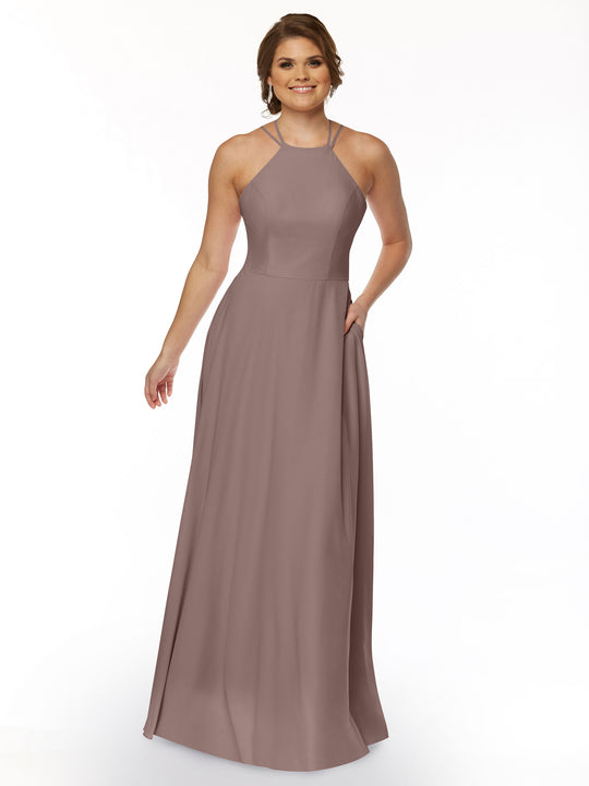 A woman models Avery Austin 83006, a sleeveless mauve A-line gown with a halter neckline and floor-length hem, smiling with one hand in the pocket against a white background.