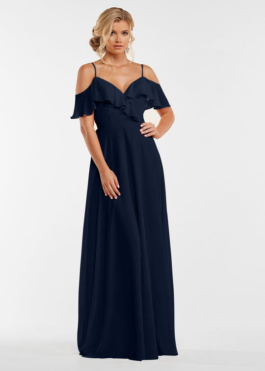 A woman models Avery Austin’s 83013, a navy blue floor-length dress with spaghetti straps, off-the-shoulder sleeves, and ruffle details against a plain white background.