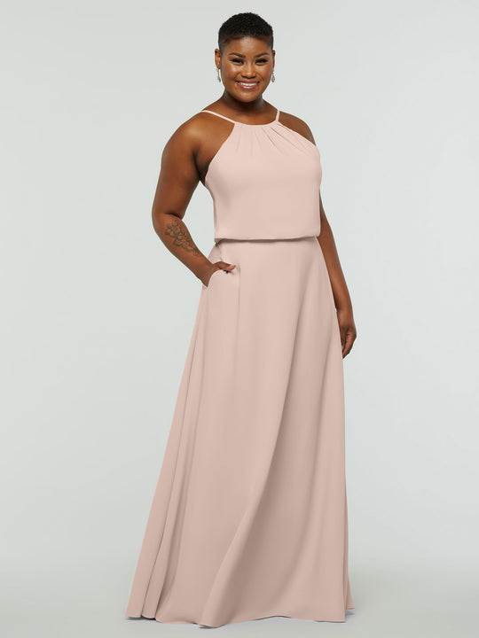 A woman smiles in the Avery Austin 83015 dress, a rose pink, floor-length A-line with a halter neck, pleated details, and spacious pockets. She has short hair, wears earrings, and poses against a plain white background.