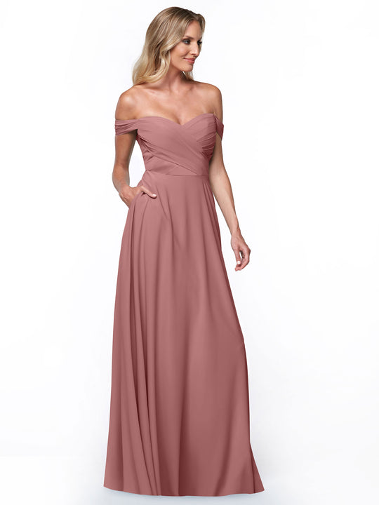 A woman models Avery Austin dress 83018, featuring a long off-the-shoulder design with a fitted ruched bodice and flowing A-line skirt, set against a plain white background.