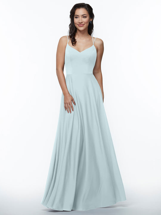 A woman wears Avery Austin's sky blue A-line dress (style 83024) with elegant double spaghetti straps, standing against a white background. She smiles softly, her right hand at her side and left hand gently on her hip.
