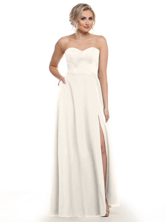 A woman stands against a plain white background wearing Avery Austin's 83025, a strapless, floor-length bridesmaid dress with a sweetheart neckline and thigh-high slit.