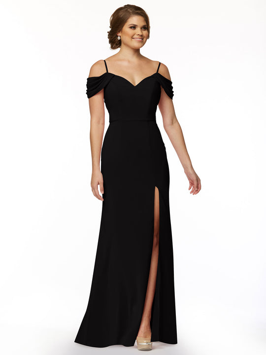 A woman models Avery Austin's fitted black off-the-shoulder dress (Style 83029) with spaghetti straps and a thigh-high slit, standing against a white background. Her light brown hair is styled up, and she completes the look with nude heels.